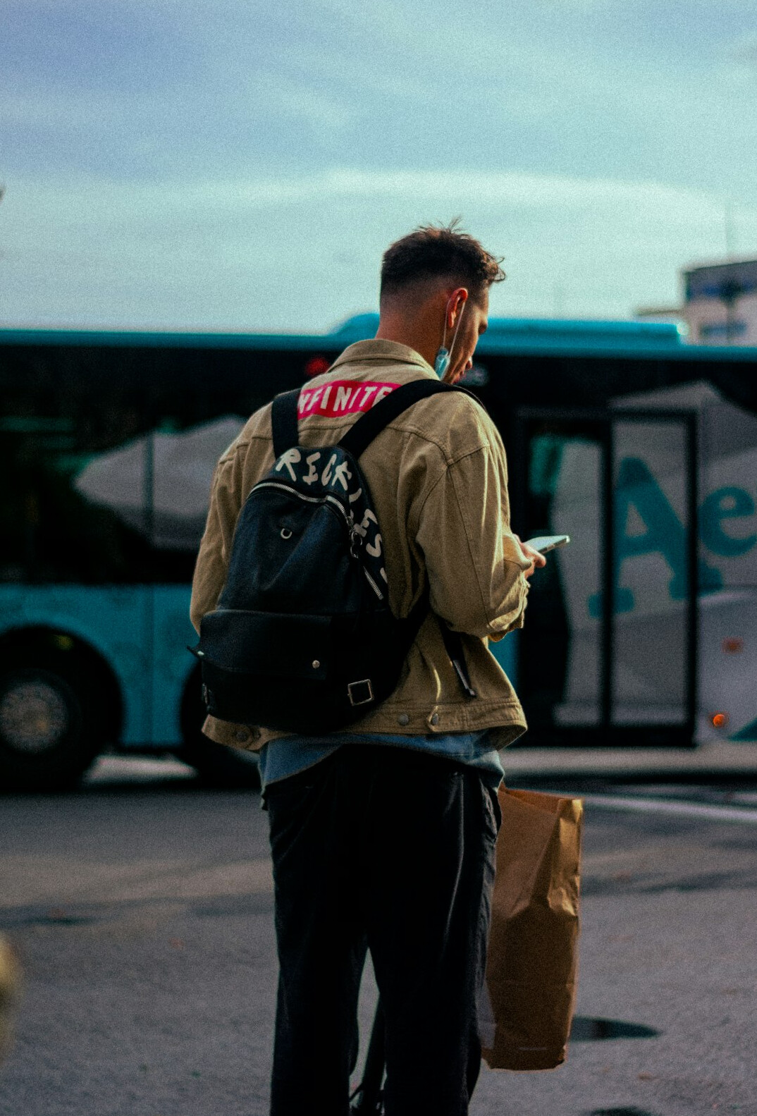 Portrait of a young commuter waiting at a bus stop with a backpack